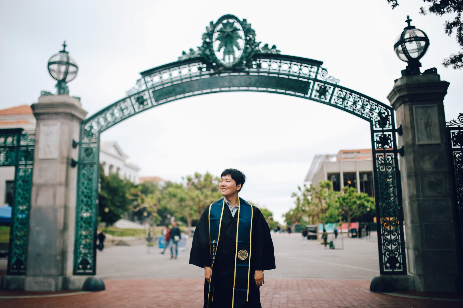 Jihun Lee in graduation gown under Sather Gate at UC Berkeley